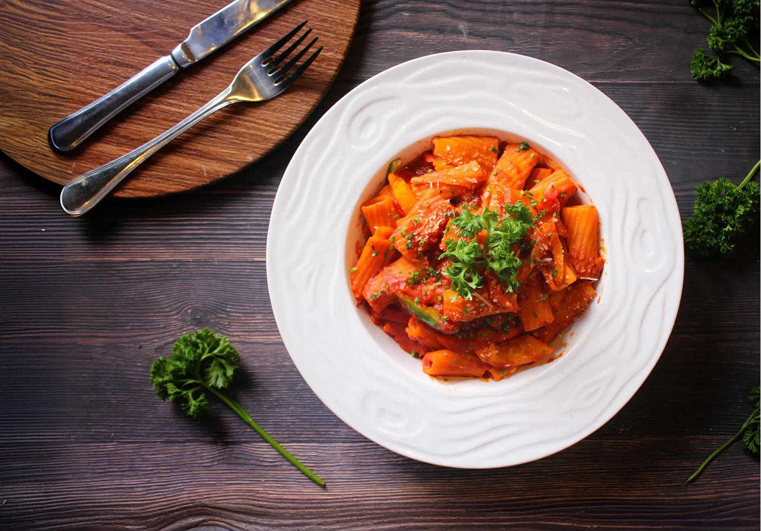 A plate of penne in tomato sauce on a wooden board